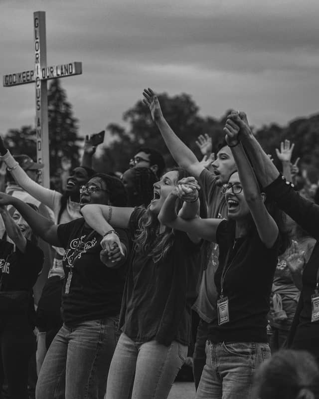 Arms raised in worship beside a cross at Jesus Festival 2026